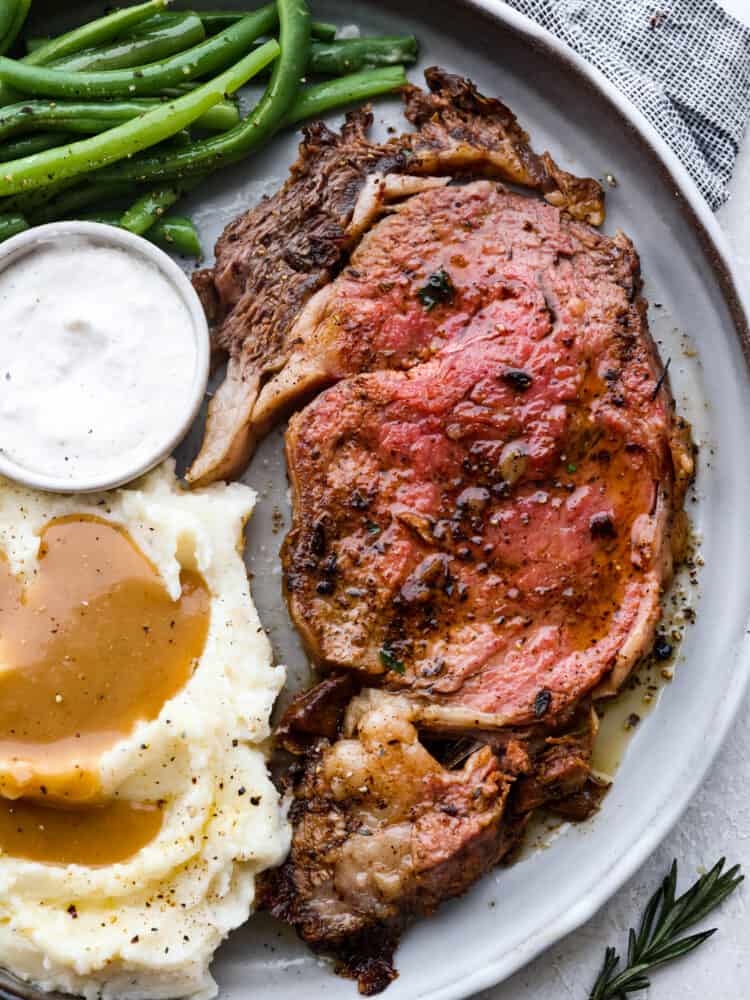 A slice of prime rib served with sauce, mashed potatoes and gravy, and broccolini.