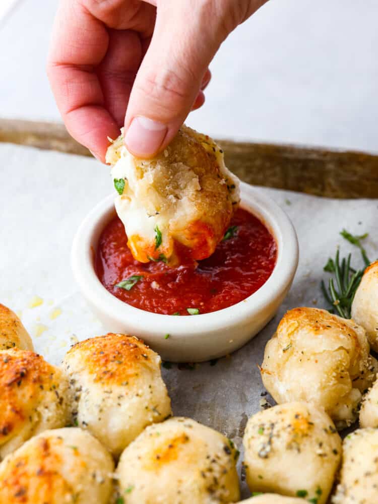 A close up of a hand dipping the roll into some marinara sauce.