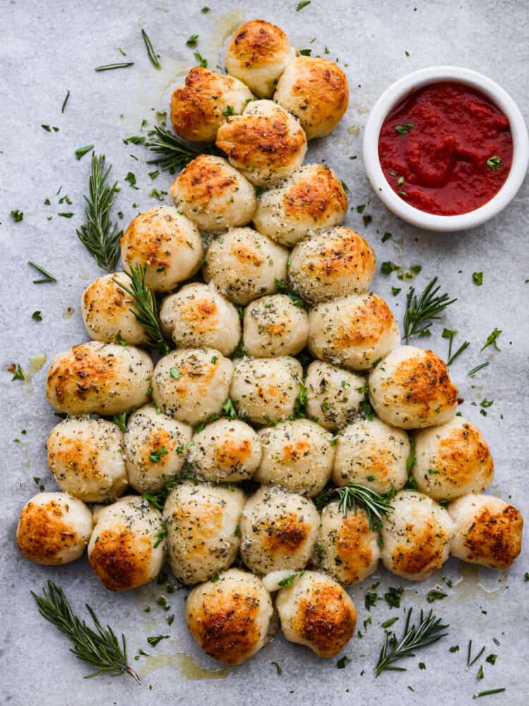 Baked pull apart bread in the form of a Christmas tree with red dipping sauce.