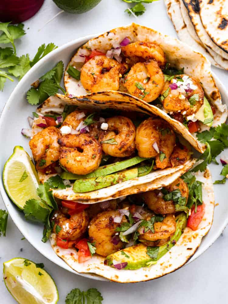 Top-down view of 3 prepared tacos on a white plate.