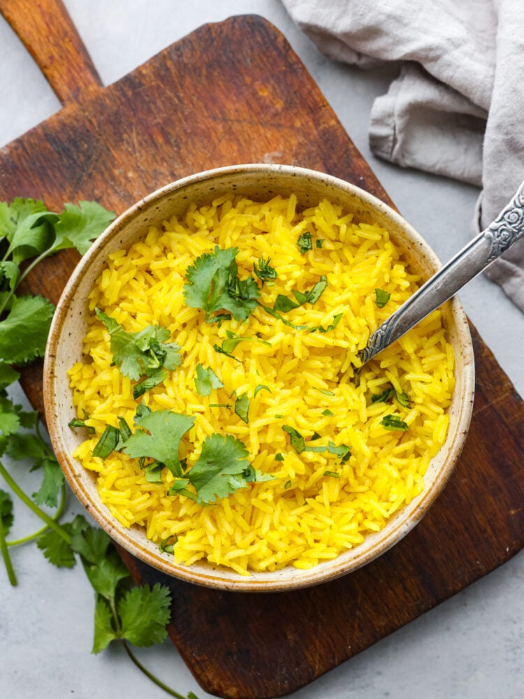 Top-down view of yellow rice in a stoneware bowl, served on top of a wooden board.