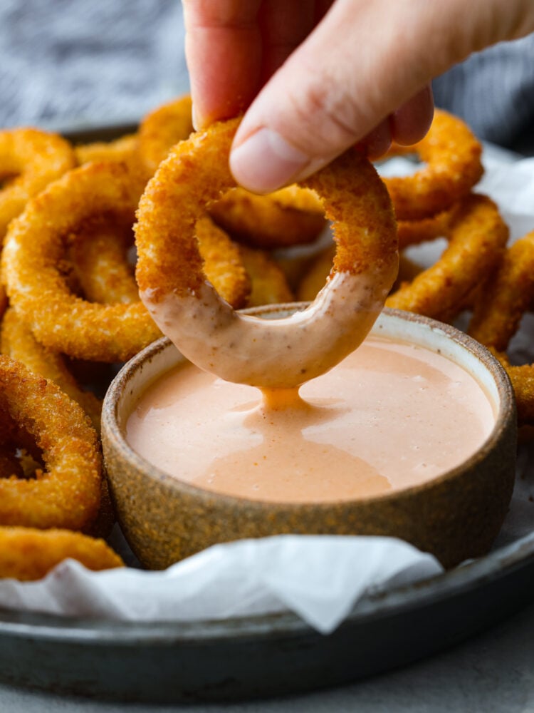 An onion ring being dipped in sauce.