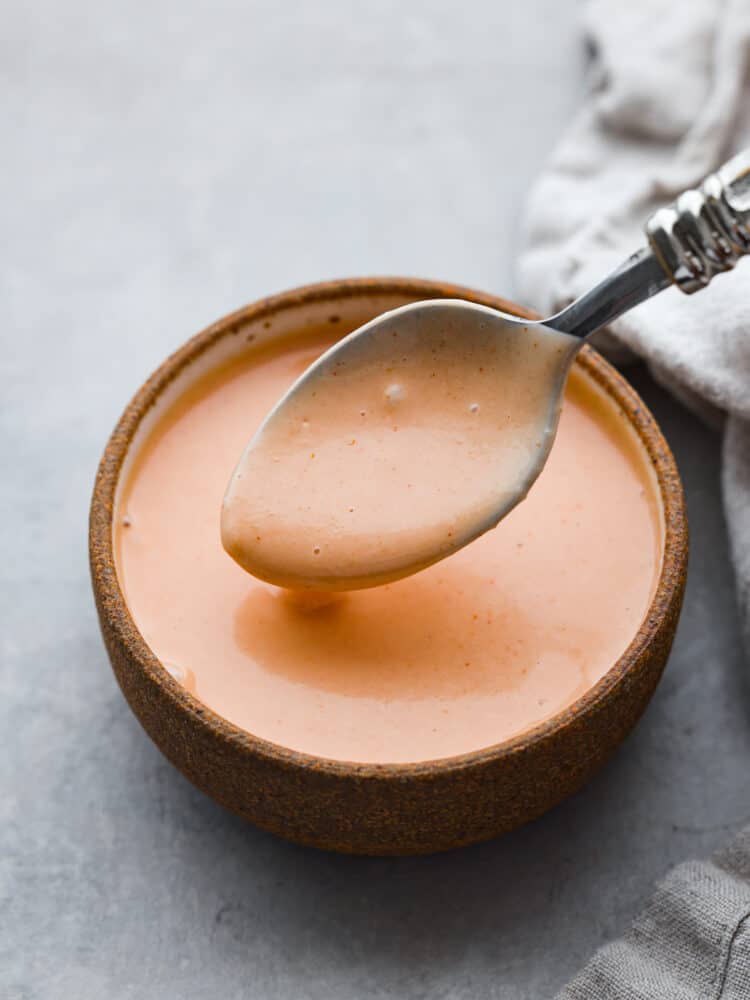 Hero image of comeback sauce in a brown stoneware bowl, being scooped up with a metal spoon.