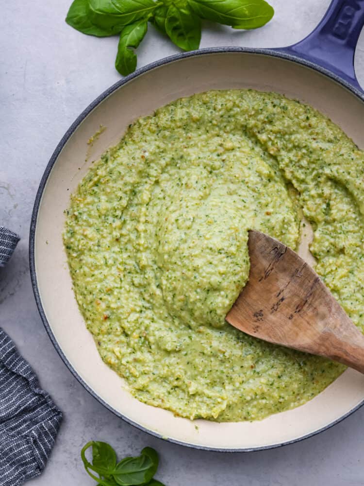 Creamy pesto in a sauce pan with a wooden spoon.