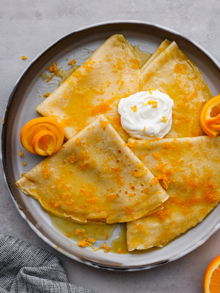 3 folded crepes covered with orange syrup and whipped cream in a skillet.