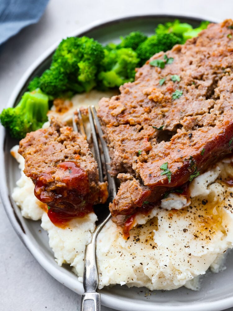 A slice of crockpot meatloaf served with broccoli and mashed potatoes.