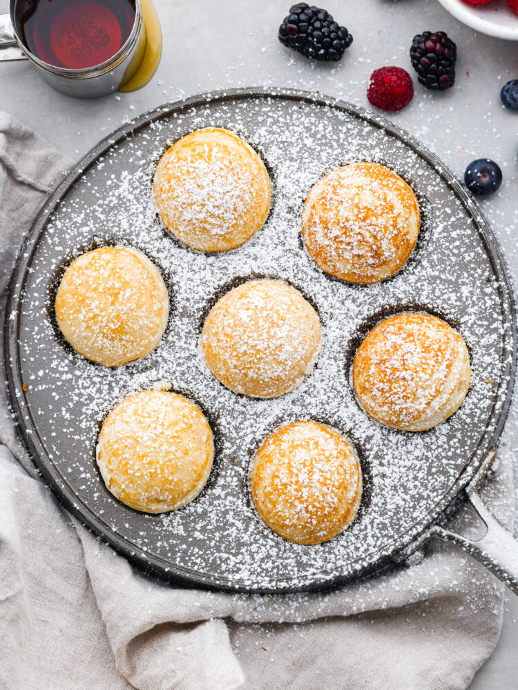 An overhead view of the ebelskivers cooked in their pan with powdered sugar on top.
