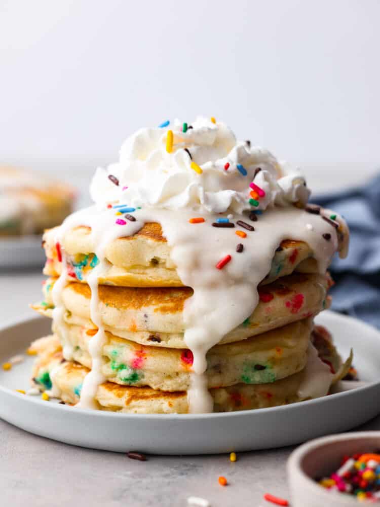 Funfetti pancakes stacked on top of each other with a glaze and whipped cream on top.