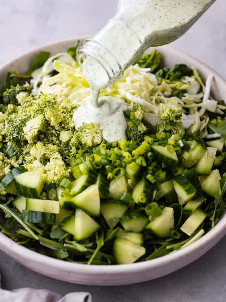 Salad dressing being poured over various greens.