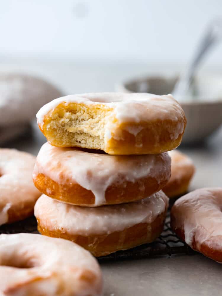 Fried glazed donuts stacked on top of each other with a bite taken out of the top one.