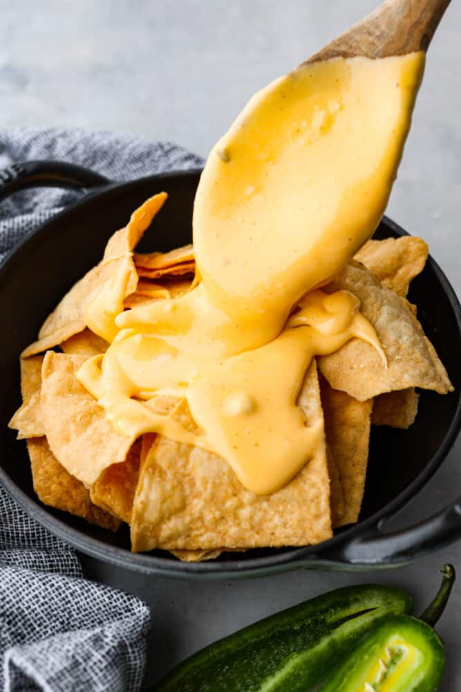 Nacho cheese being poured over tortillas.