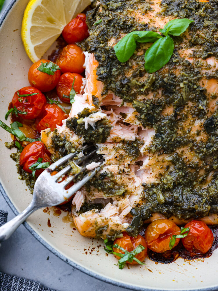 A delicious and flaky pesto salmon fillet in a pan being pulled apart by a fork.