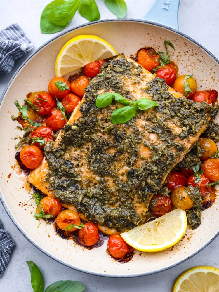 Pesto salmon in a pan with tomatoes lemons and fresh basil.