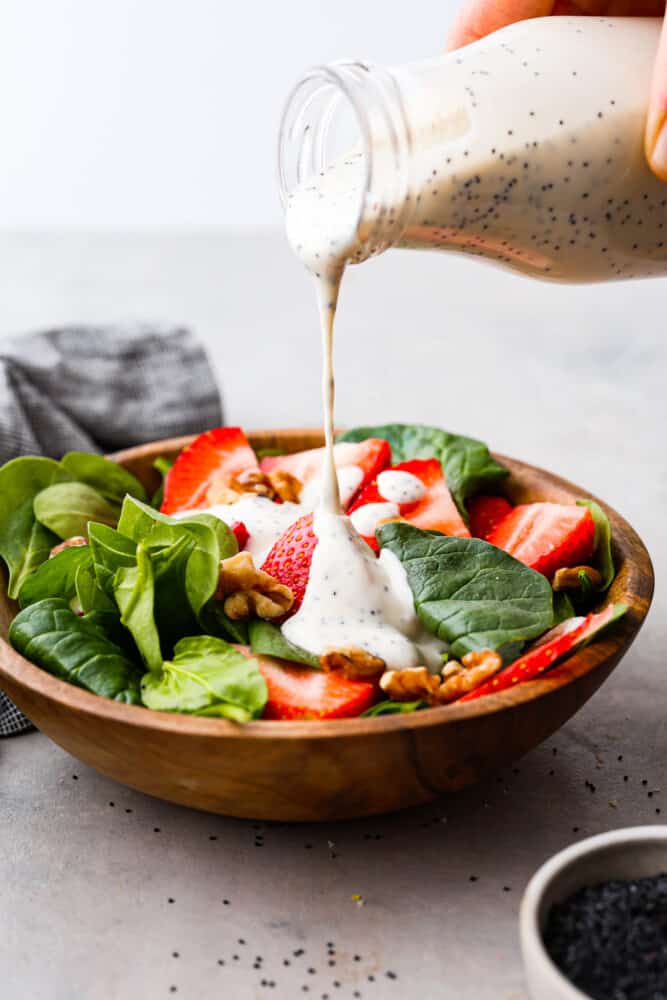 Creamy poppyseed dressing being poured over the top of a fresh salad.
