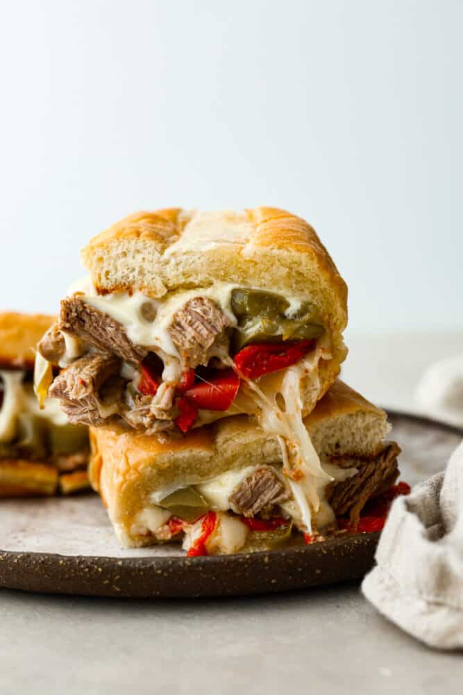 Slow cooker philly cheesesteak sandwiches stacked on top of each other.