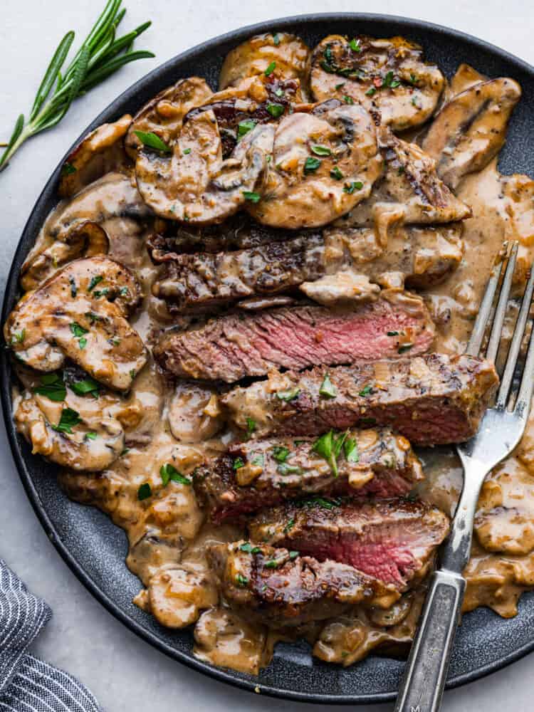 Steak diane on a plate with strips of beef cut up and a fork to the side.