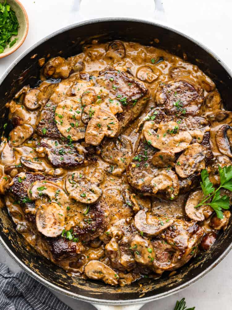 An overhead view of steak diane on a black plate.