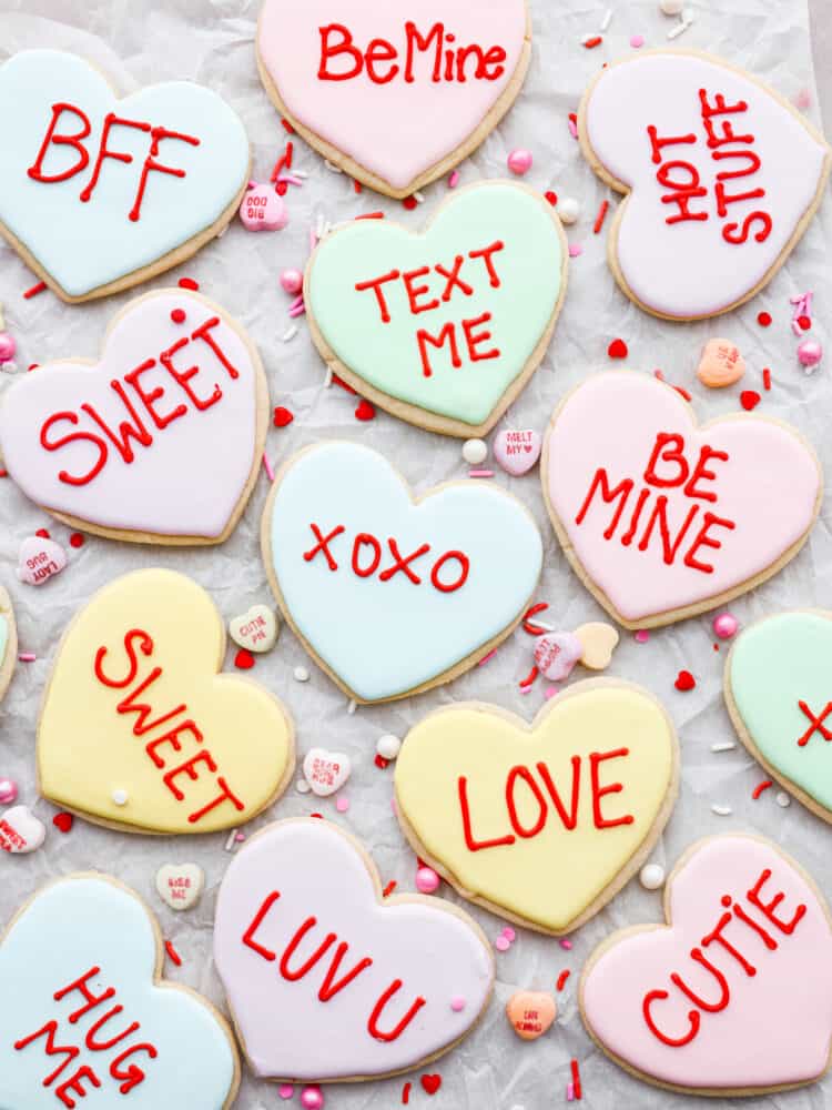 An overhead view of all the Valentine's Day cookies on parchment paper with the conversation hearts next to them.