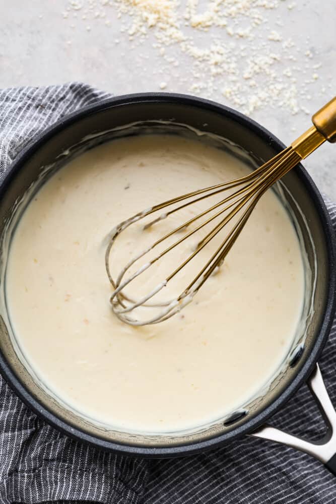 A whisk in a bowl of the white pizza sauce.
