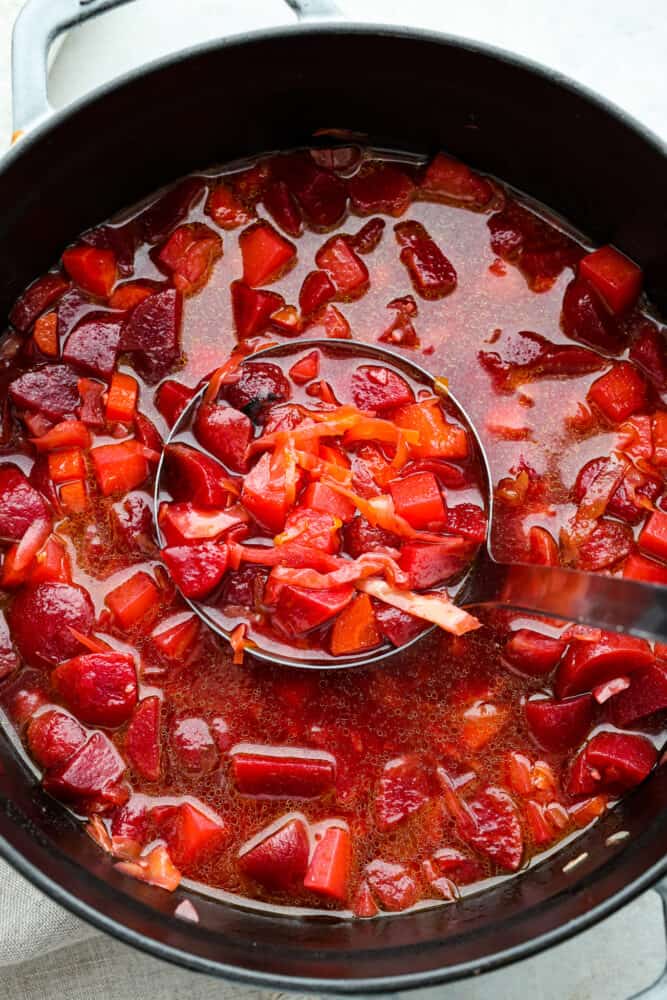 Top-down view of borscht being scooped up with a ladle in a large pot.
