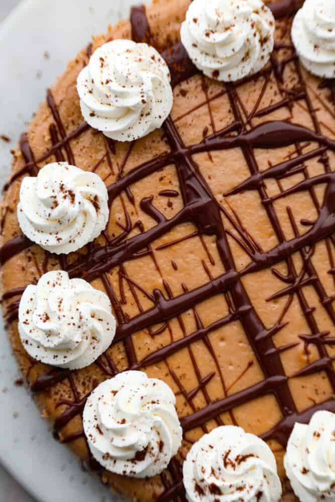 Top-down view of Bailey’s cheesecake topped with whipped cream and chocolate ganache drizzle.