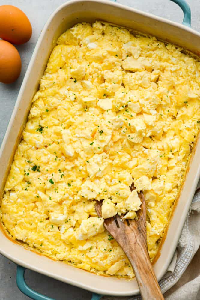 Baked scrambled eggs in a casserole dish with a wooden spoon.