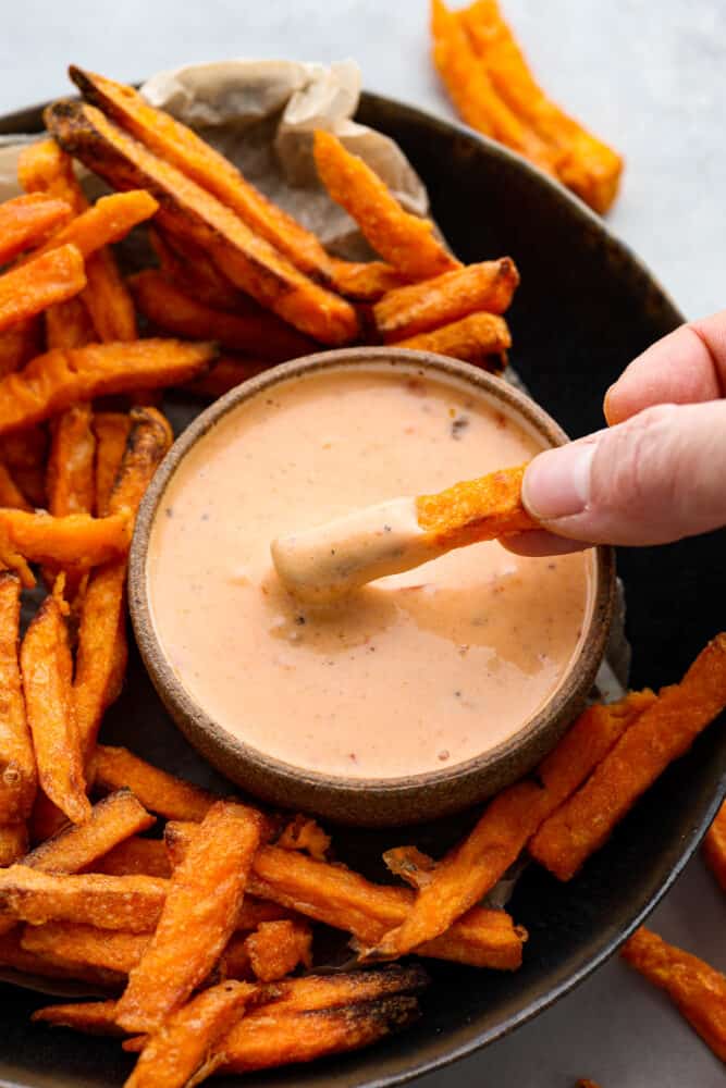 Eine Hand, die eine Pommes Frites in die Boom-Boom-Sauce taucht.