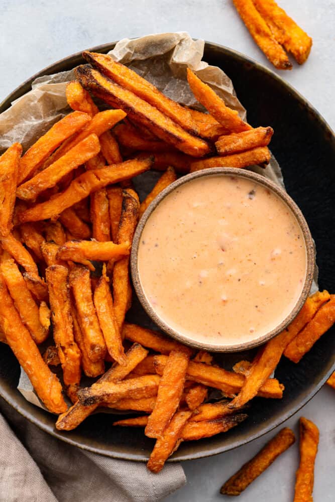 A bowl of sauce with french fries around it.