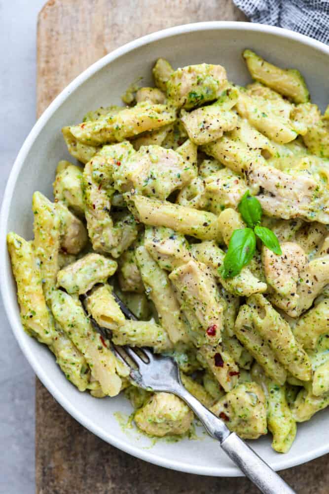 A close up on chicken pesto pasta in a white bowl.