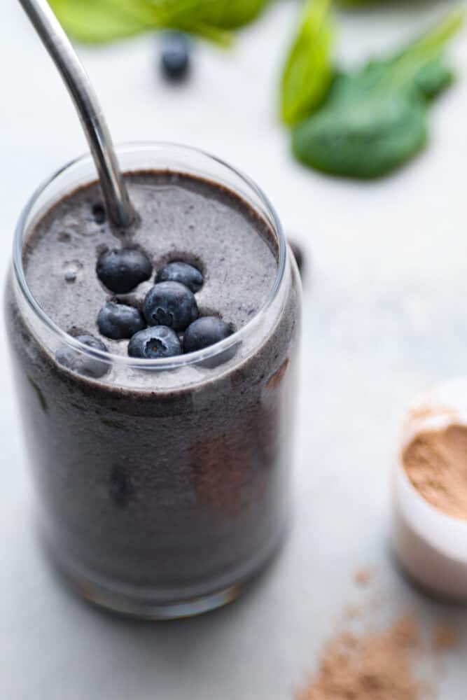 A close up on a blueberry protein smoothie with a metal straw.