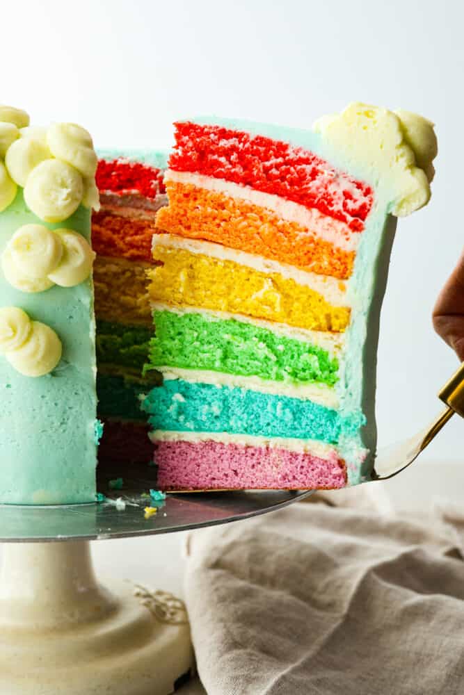 Serving a piece of rainbow cake with a cake spatula.
