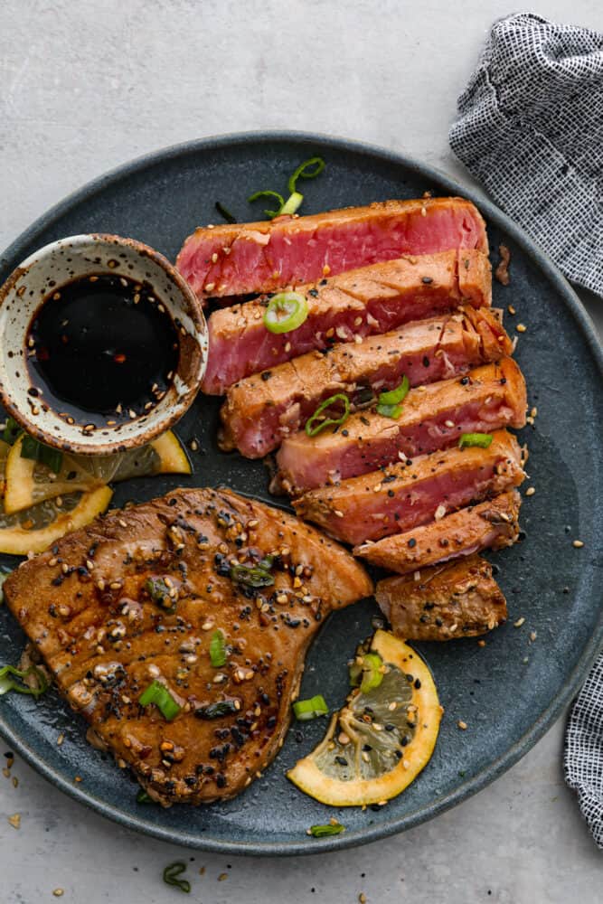 Seared ahi tuna steak on a plate cut up with a dipping sauce.