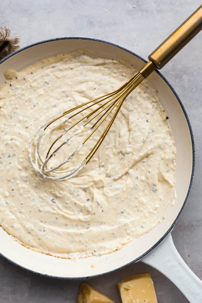 Top-down view of alfredo sauce being whisked in a blue and white skillet.