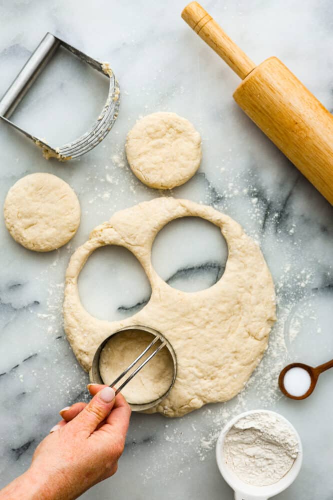 A hand holding a biscuit cutter cutting the biscuit dough.