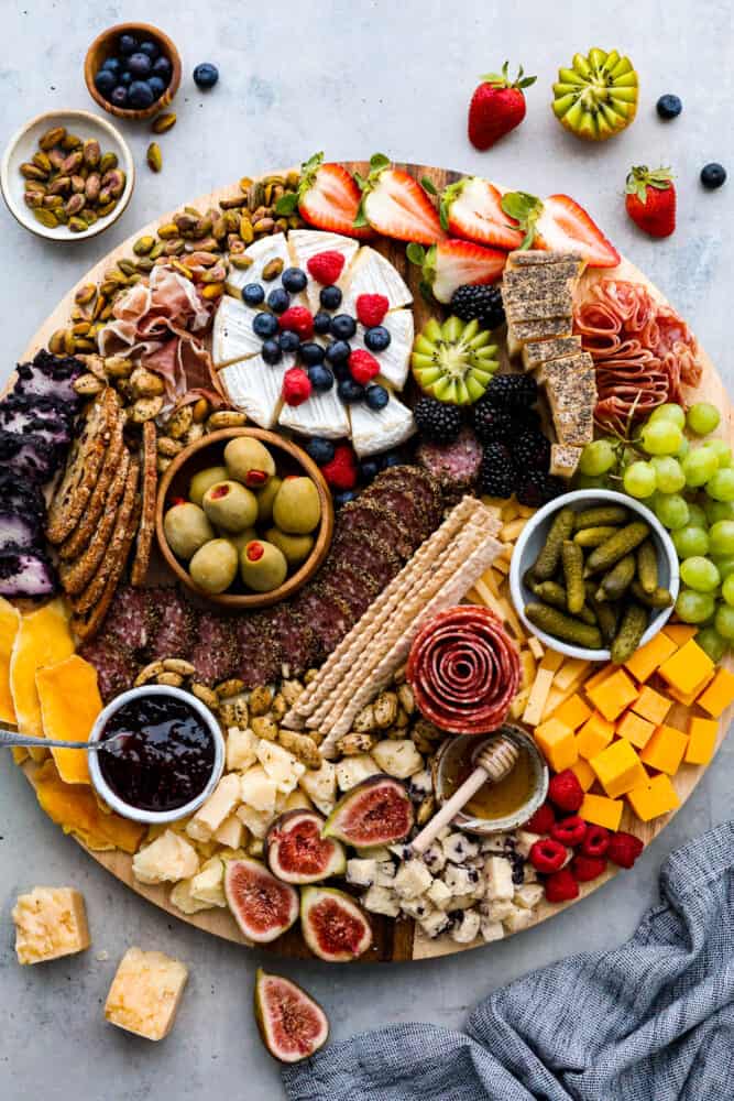 Hero image of a charcuterie workbench topped with various cheese, fruit, meats, nuts, and crackers.