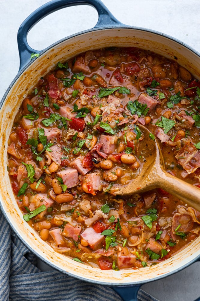 Charro beans in a pot with a wooden spoon.