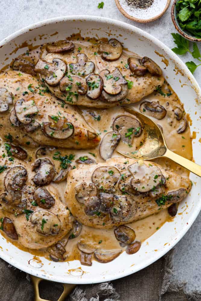 Creamy Chicken Marsala is a classic Italian dish that is ready in under 30 minutes! Marsala wine is made into a creamy sauce paired with mushrooms for the ultimate savory bite. It's simple and easy to whip up and sure to be a crowd-pleaser! Creamy chicken marsala on a plate with a golden spoon.