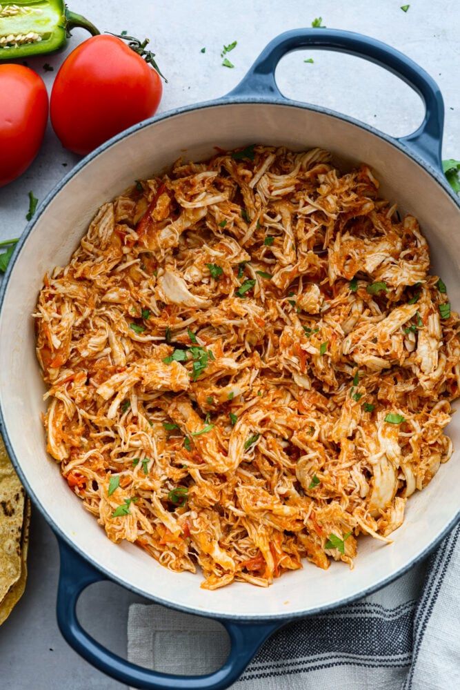 Chicken tinga in a white and blue skillet.