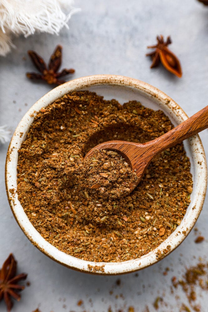 Chinese five spice blend in a bowl with a wooden spoon.