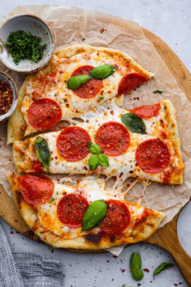 Flatbread pizza is a simple and delicious recipe that is easier to make than regular pizza. With a thin and chewy flatbread crust that is topped with your favorite pizza toppings, it's even better than takeout and always a hit! Flatbread pizza cut into three pieces.