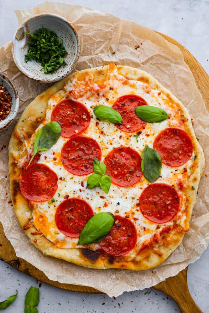 Flatbread pizza is a simple and delicious recipe that is easier to make than regular pizza. With a thin and chewy flatbread crust that is topped with your favorite pizza toppings, it's even better than takeout and always a hit! Flatbread pizza on a piece of parchment with fresh basil on top.