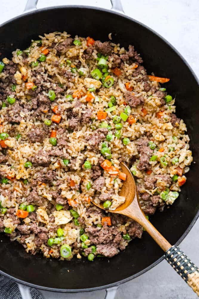 Beef fried rice in a pan with a wooden spoon sticking out of it.