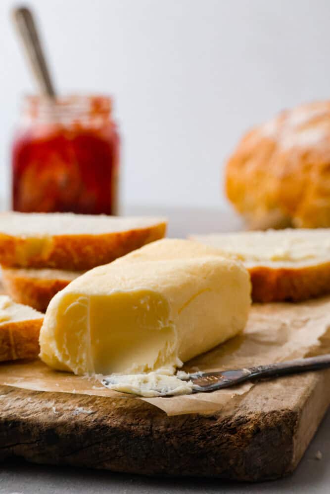 Homemade butter on a cutting board with bread in the background.