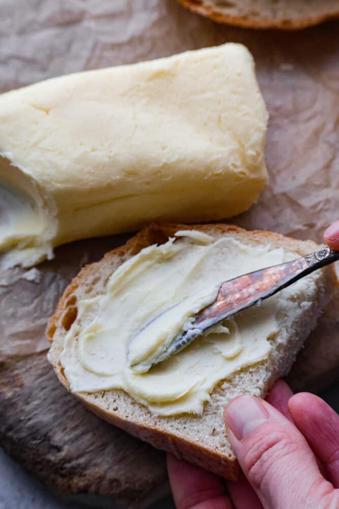 A hand spreading butter onto a piece of bread with a butter knife.