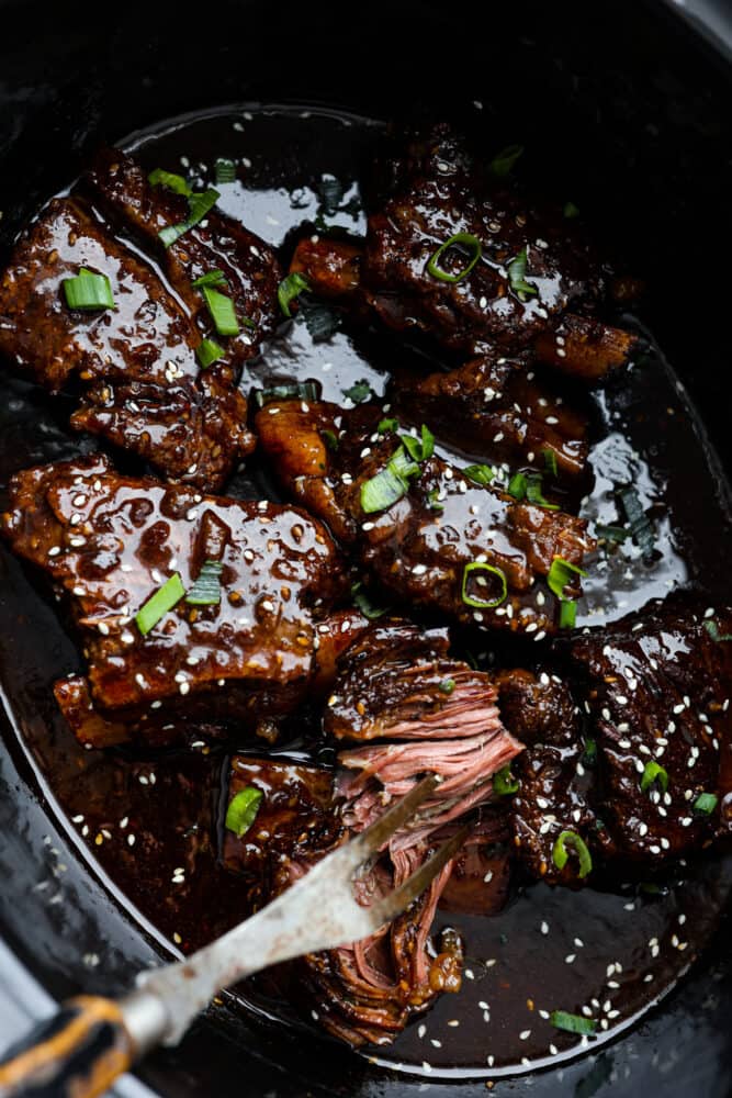 A close up on the short ribs in the slow cooker being pulled apart.