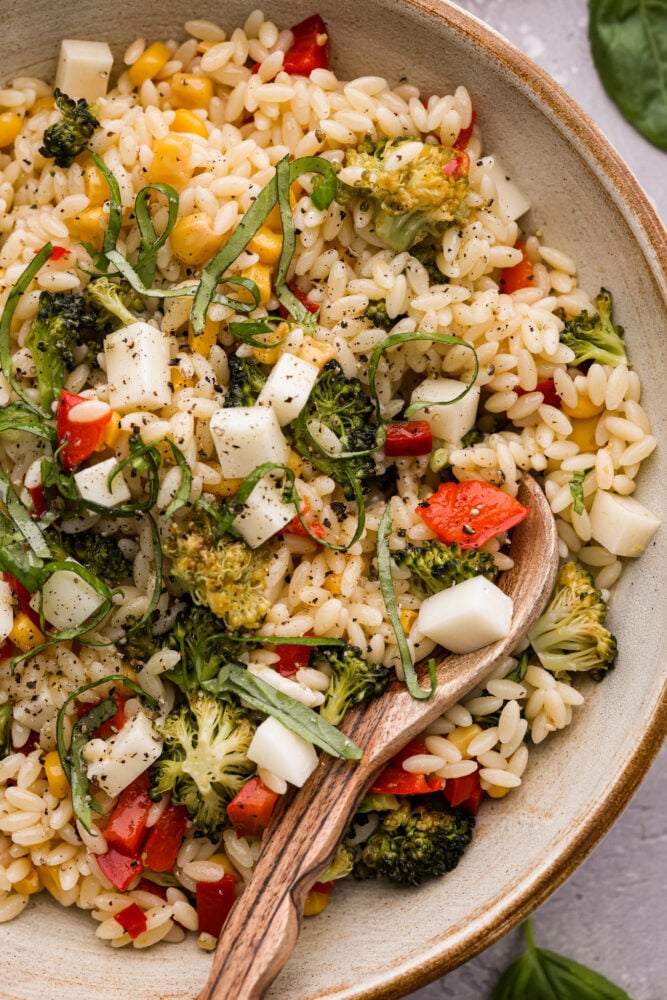 A close up on orzo pasta salad with a wooden spoon.