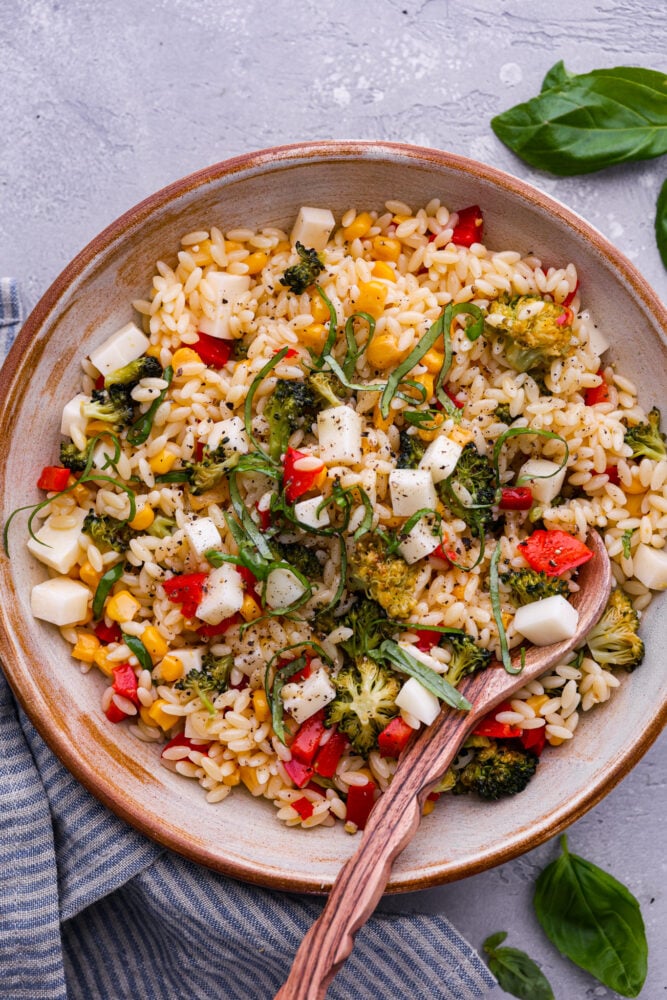 Orzo pasta salad in a bowl with a wooden spoon.