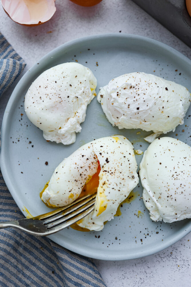 Poached eggs on a plate with a fork cutting into one of them