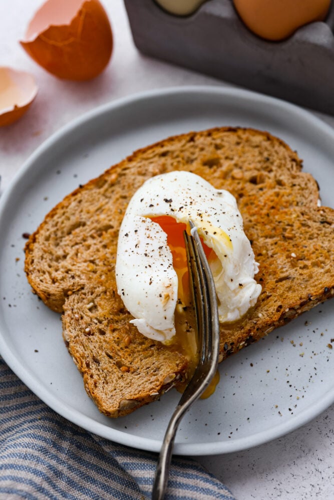 A poached egg being cut open on top of a piece of toast by a fork.