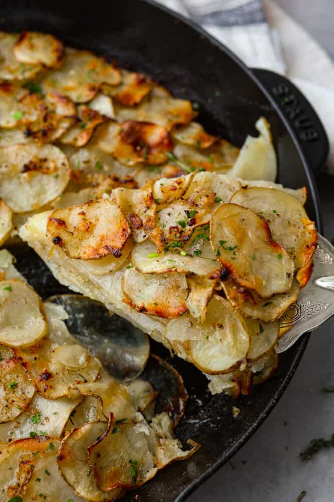 Potato galette is a beautiful side dish made up of thinly sliced potatoes seasoned to perfection and baked until crispy on top and creamy in the middle. They are next-level delicious and really easy to make at home! A slice of potato galette being lifted out of the cast iron skillet.